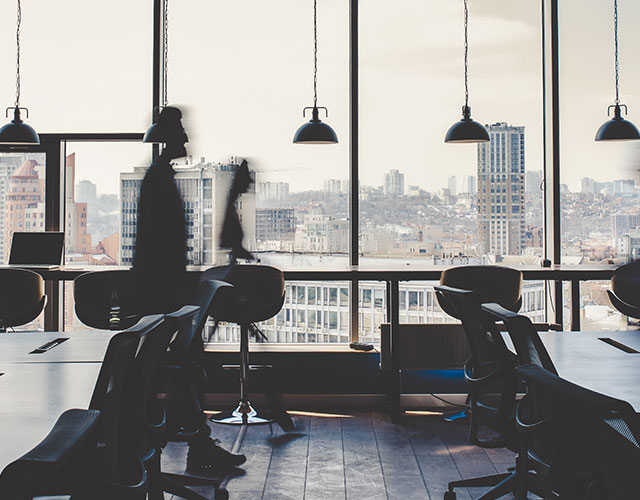 Silhouettes of people moving through a modern office with city views.
